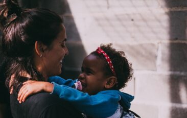 Una mujer sostiene en brazos a un niño pequeño que lleva una chaqueta azul y se ríe.