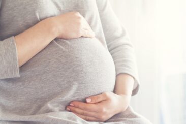Eine Frau hat ihre Hände auf ihrem schwangeren Bauch.